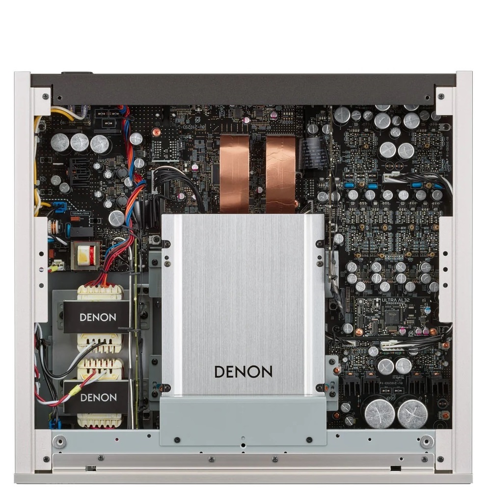 Internal view of a Denon amplifier showing the power supply with a large silver transformer, copper inductors, and dense circuit boards online.