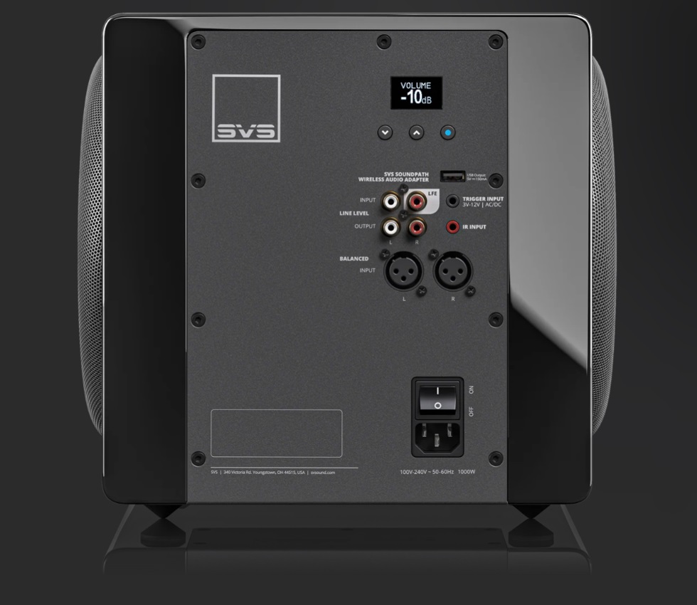 Back panel of a SVS wireless audio adapter showing inputs, outputs, and power switch on a dark subwoofer/speaker unit in a home theater setup